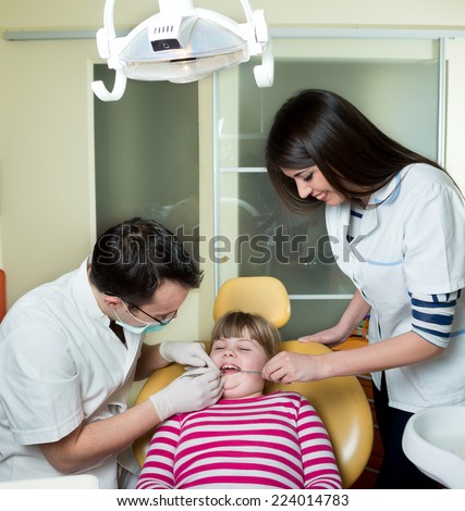 little girl to the dentist in the dental chair sits next to a doctor to do the dentist to see if his teeth were okay/little girl to the dentist