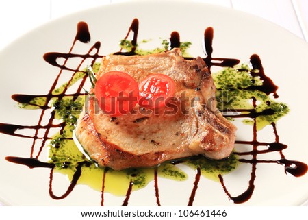 Pan fried pork chop decorated with pesto sauce and balsamic drizzle