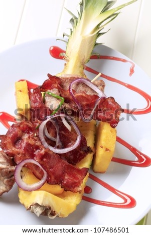 Meat skewers and crispy bacon strips on pineapple