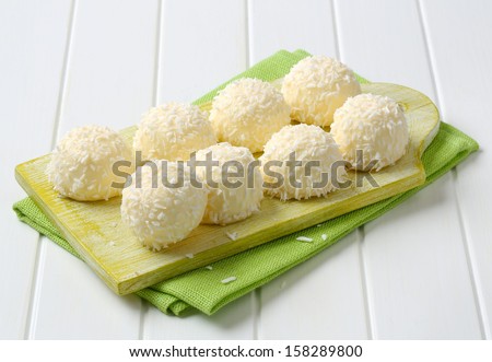 eight white chocolate pralines breaded in grated coconut, on a wooden board