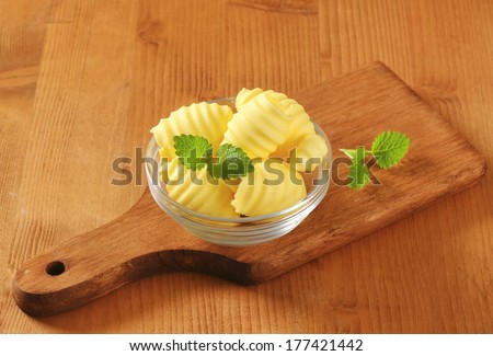 portioned butter curls in served in a glass bowl with wooden cutting board
