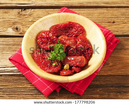 dried tomatoes pickled in oil with herbs, served in a wooden bowl with napkin