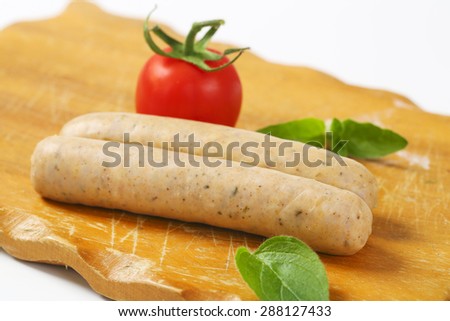 close up of white sausages, fresh basil and cherry tomatoes on wooden cutting board