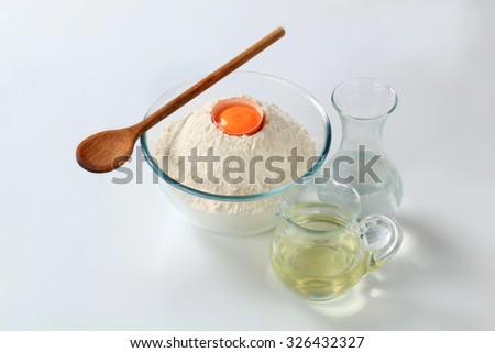 bowl of flour with yolk, carafe of water and jug of cooking oil