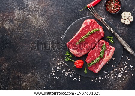 Two raw steak New York with rosemary and spices. Flat lay top view on black stone cutting table.