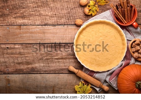 Dough for baking quiche, tart or pie in ceramic baking form ready for bake on kitchen towel over old rustic plank wooden background. Top view, copy space. Concept homemade baking for holiday.