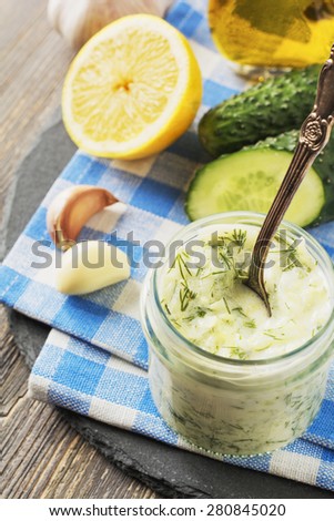 Fresh tzatziki in glass jar with cucumber, lemon,garlic and olive oil on an old wooden table background.Selective focus.