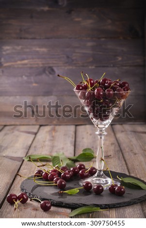 Fresh ripe cherries in transparent clear wineglass on old wooden table background.Selective focus.Retro style toned.