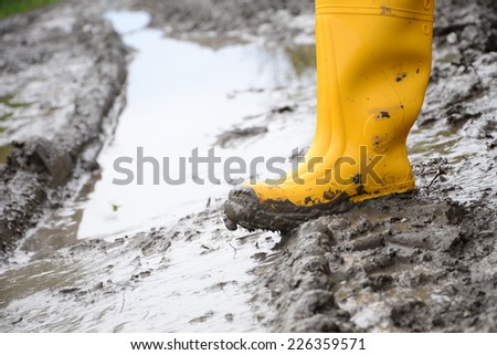 Human leg with Yellow Muddy rubber boots on wet silt