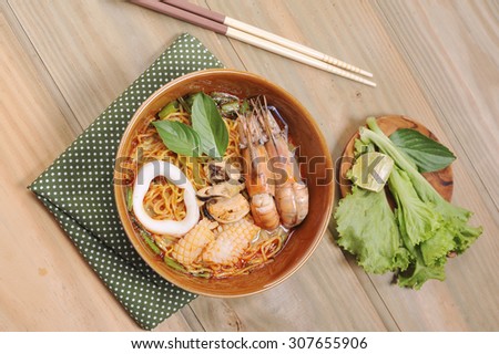 Tom Yam Kung soup with noodles , Tom Yum Nam Khon - Creamy Thai soup with prawns and mushrooms garnished with coriander leaves and served with lime wedges. Overhead shot.