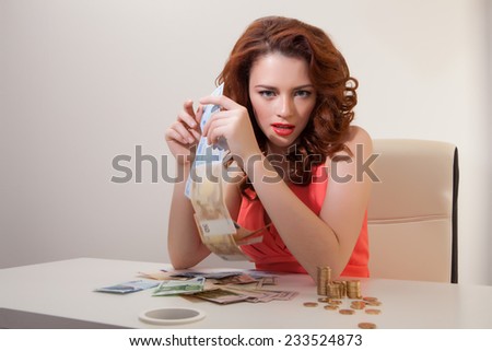 young girl at table with greedy counts the money lying on table and looking at  camera