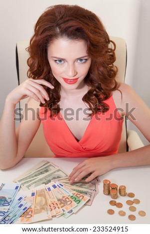 young girl at table with greedy countsmoney lying on table and looking at  camera