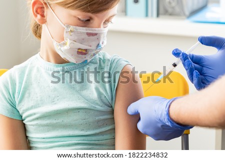 Little girl in face mask in doctor's office is vaccinated. Syringe with vaccine for covid-19 coronavirus,flu,dangerous infectious diseases. Injection after clinical trials for human, child. Medicine.