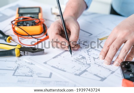 Man repairer making electricity project in house.Repairs planning.Drawing,diagrams,plan of electrification of apartment,building.Devices,accessories,voltmeter,wires,screwdriver,pliers and tape measure