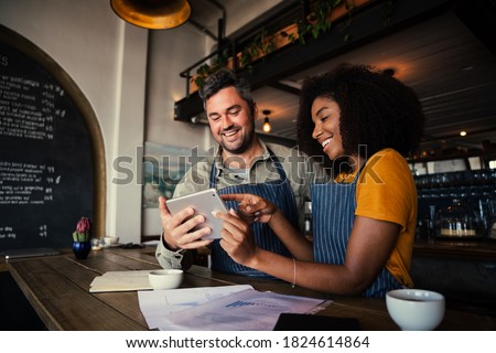 Manager and waitress laughing at designs on digital tablet standing with hot coffee in cafe  商業照片 © 