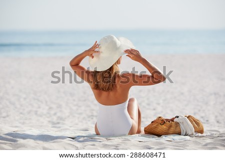 Attractive woman looking at view sitting on beach wearing one piece bathing suite