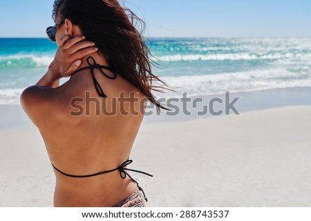 Sexy woman wearing colorful bikini detail shot from behind showing back of body with perfect tropical ocean background