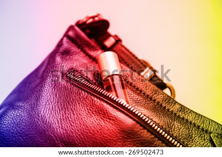 Small perfume bottle sticking out of the unzipped pocket black handbags, lying on the table