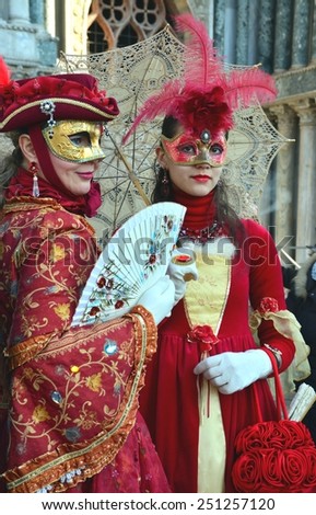 VENICE, ITALY-FEBRUARY 8: An unidentified couple of women dress red fancy dresses with masks, white gloves and red feather hats during Venice Carnival at Piazza San Marco on February 8, 2015 in Venice