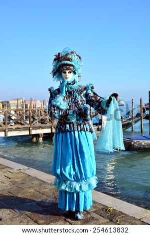 VENICE, ITALY â?? FEBRUARY 8:An unidentified man dresses an azure fancy dresses.Man has white masks and stands near the Venetian lagoon during Carnival at Piazza San Marco on February 8, 2015 in Venice