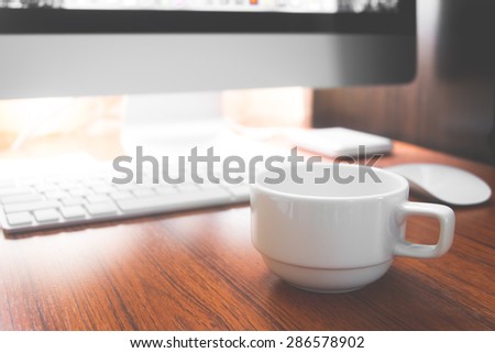 Cup of coffee and PC on wooden desk vintage color