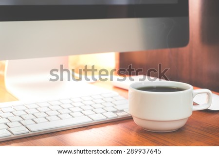 Cup of coffee and PC on wooden desk vintage color