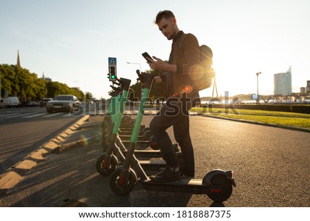 Young man unlocks an e-scooter with his mobile phone. Electric scooter new way city mobility. Green transportation. Sustainable climate neutral cities goals. Green mobility sustainable transportation
