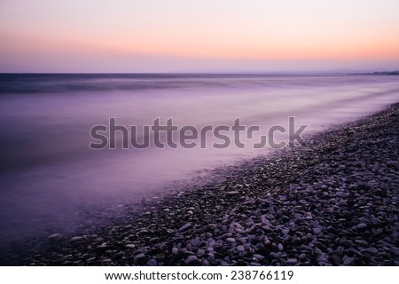 Sea long exposure of sea and rocks. Purple and pink sunset. Pebble beach, foggy water.