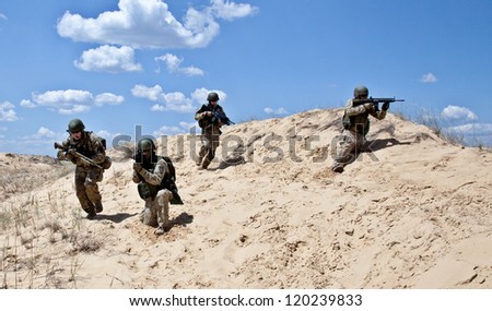 Squad of soldiers run through the desert through the military operation