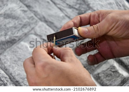 Detail of ignition of matches for a matchbox. A match in one hand and a matchbox in the other. The process of lighting a match. Hand with a match, the match has not yet been lit on a gray background