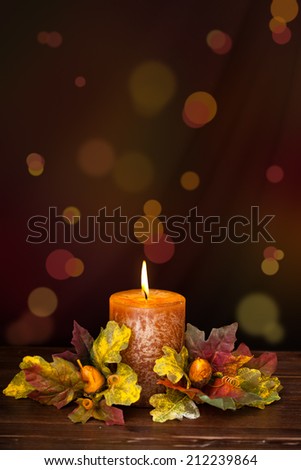 Autumn arrangement with candle against de-focused holiday lights.
