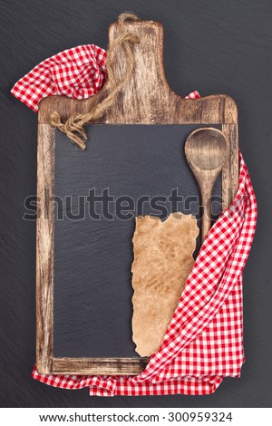 Cutting board, tablecloth, wooden spoon and piece of old paper for recipe. Over dark slate board.