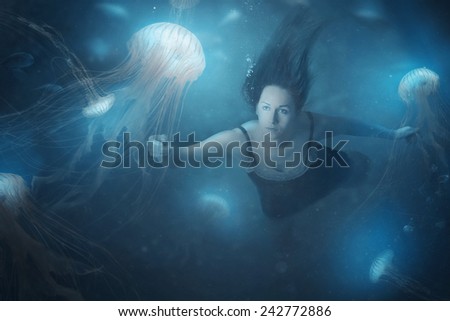 A woman swimming in the deep ocean with jelly fish
