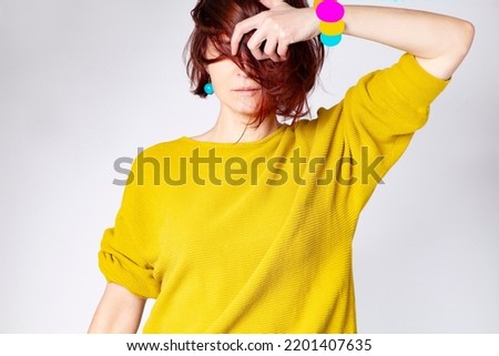 Beautiful woman with short dark hair and yellow sweater, blue earrings and digitally made bracelet isolated on a white background. Face partly covered. Foto stock © 