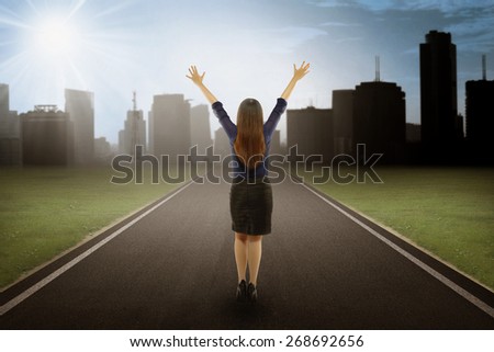 Back view of businesswoman showing happy body in positive mind on the road to reach a goal near the city view