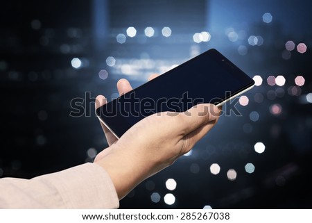 Hand holding cellphone with blank screen on blurry night city. You can put your design on the cellphone
