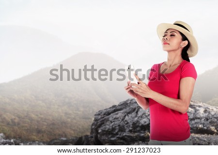 Asian tourist wearing hat holding cellphone at the mountain
