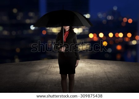 Business woman holding umbrella standing on the rooftop of the building at night time