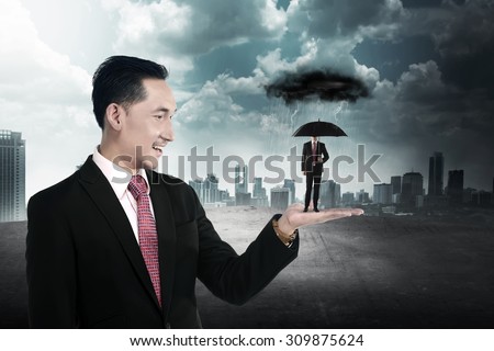 Business man holding small man using umbrella to protect himself from storm