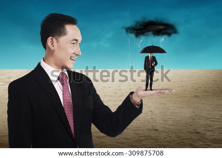 Business man holding small man using umbrella to protect himself from storm