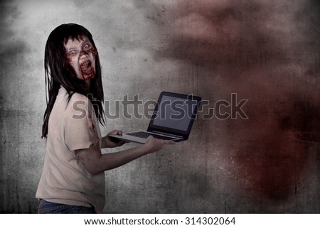 Creepy female zombie typing with laptop over grunge background