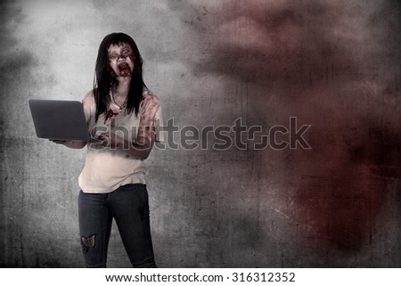 Female zombie holding laptop over grunge background. Halloween concept