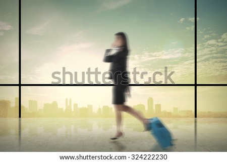 Business woman walking with suitcase over city background. Motion blur effect