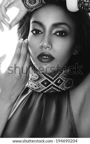 Black and white fashion portrait of the beautiful mulatto with dark skin, hair and red lips in traditional ethnic accessories, and bracelet on her hand