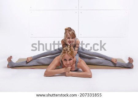 Mother daughter doing yoga exercise,fitness family sports, sports paired woman sitting on the floor stretching his legs apart in different directions pose child sits on top of the twine in  same pose