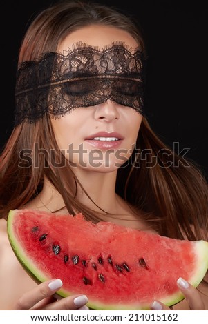 Young beautiful sexy woman with dark lace on eyes bare shoulders and neck, holding watermelon to enjoy the taste and are dieting, feeling temptation, teeth passion sexy lips