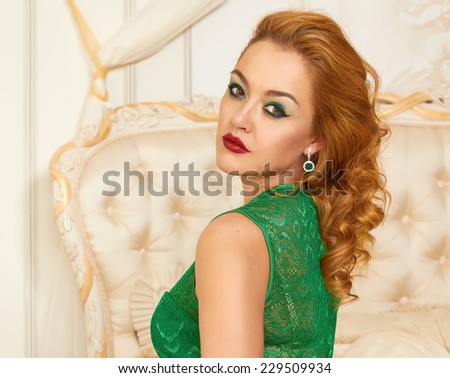 Beautiful young red-haired curly woman with bright makeup crimson lipstick,  wearing a long bright designer evening dress