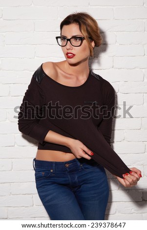 Beautiful sexy young woman with blond hair matched up with an evening make-up natural red lipstick in stylish glasses for vision wearing a black T-shirt and jeans clothed thigh ideal body shape