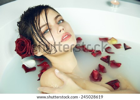 Beautiful young sexy woman with dark hair wet, evening makeup, takes bath with milk and rose petals and candles, beauty salon and spa Valentine\'s Day