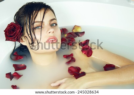 Beautiful young sexy woman with dark hair wet, evening makeup, takes bath with milk and rose petals and candles, beauty salon and spa Valentine's Day